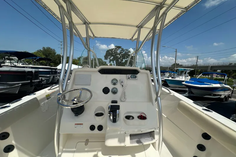 Slide: The Image of 2023 Sailfish 242 CC boat console with steering wheel and controls, docked under clear sky. - 14
