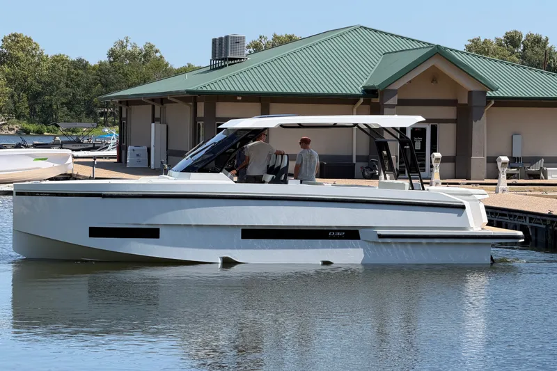 Slide: The Image of 2027 De Antonio Yachts D32 docked at marina, modern design, green-roofed building in background. - 2