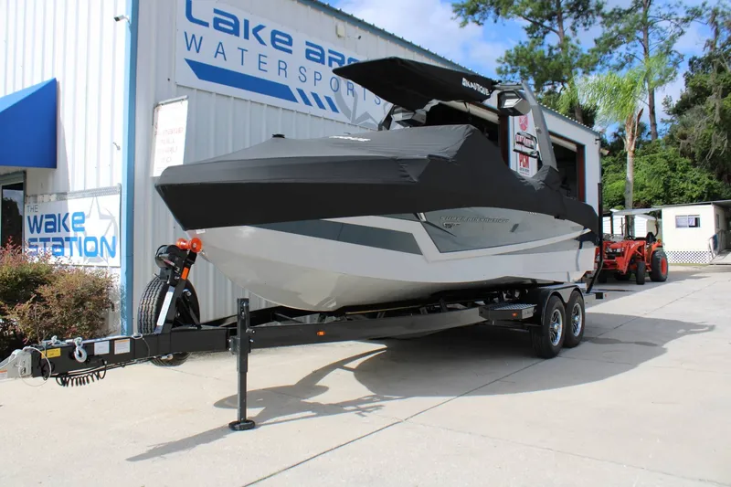 Slide: The Image of A 2027 Nautique Super Air Nautique S23 boat on a trailer outside a watersports shop. - 16