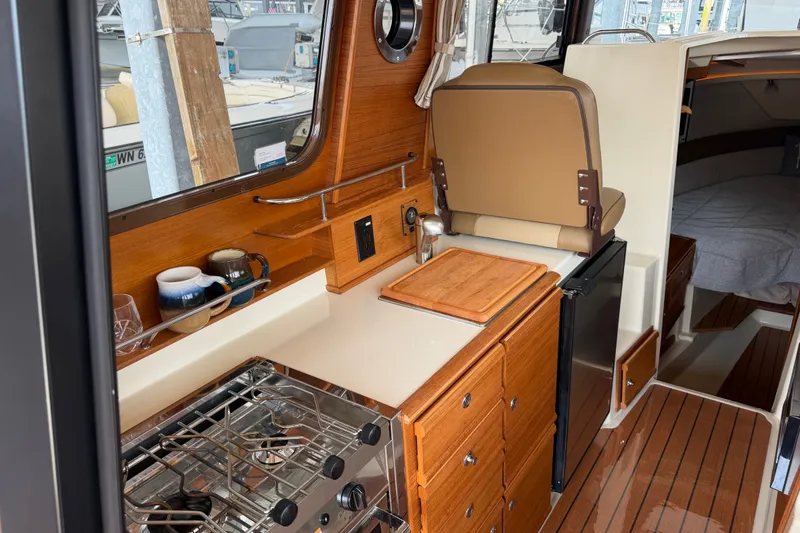 Slide: The Image of 2024 Ranger Tugs R-27 interior with kitchenette, stove, and cozy cabin space. - 22