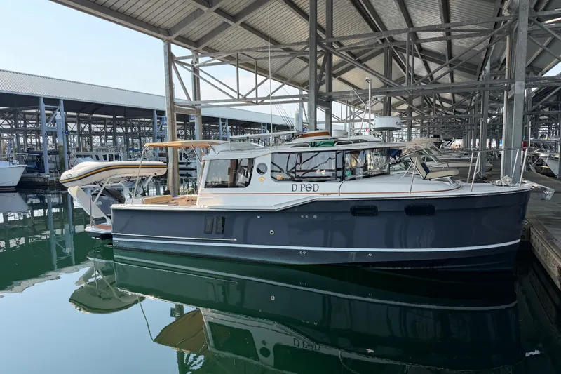 The Image of 2024 Ranger Tugs R-27 boat docked in a marina under a covered structure. - 0
