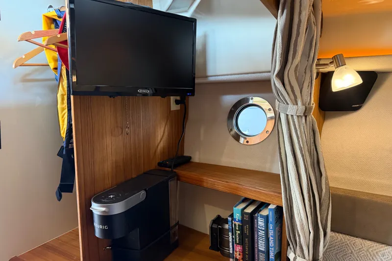 Slide: The Image of 2024 Ranger Tugs R-27 cabin interior with TV, coffee maker, books, and porthole. - 43