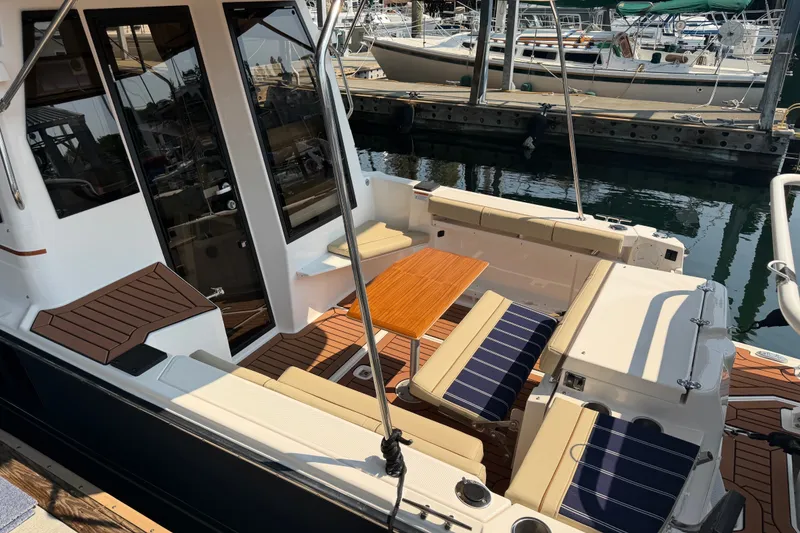 Slide: The Image of 2024 Ranger Tugs R-27 boat interior with seating and wooden table at marina. - 1