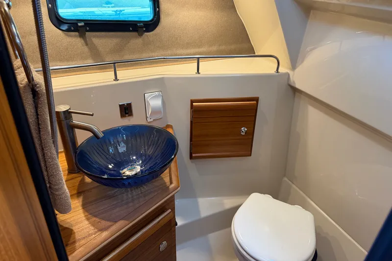 Slide: The Image of 2024 Ranger Tugs R-27 bathroom with blue glass sink and wooden cabinetry. - 44