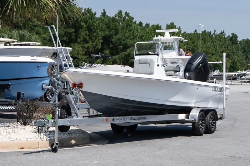 Slide: The Image of 2027 Blazer PureBay 2400 boat on trailer, parked outdoors near other boats. - 2