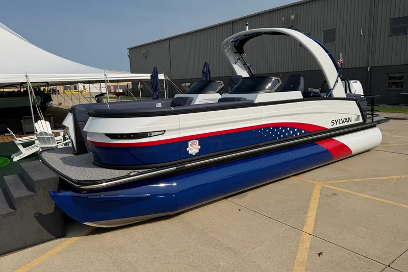 Slide: The Image of 2027 Sylvan G5 LZ DC pontoon boat with patriotic design, displayed outdoors. - 2