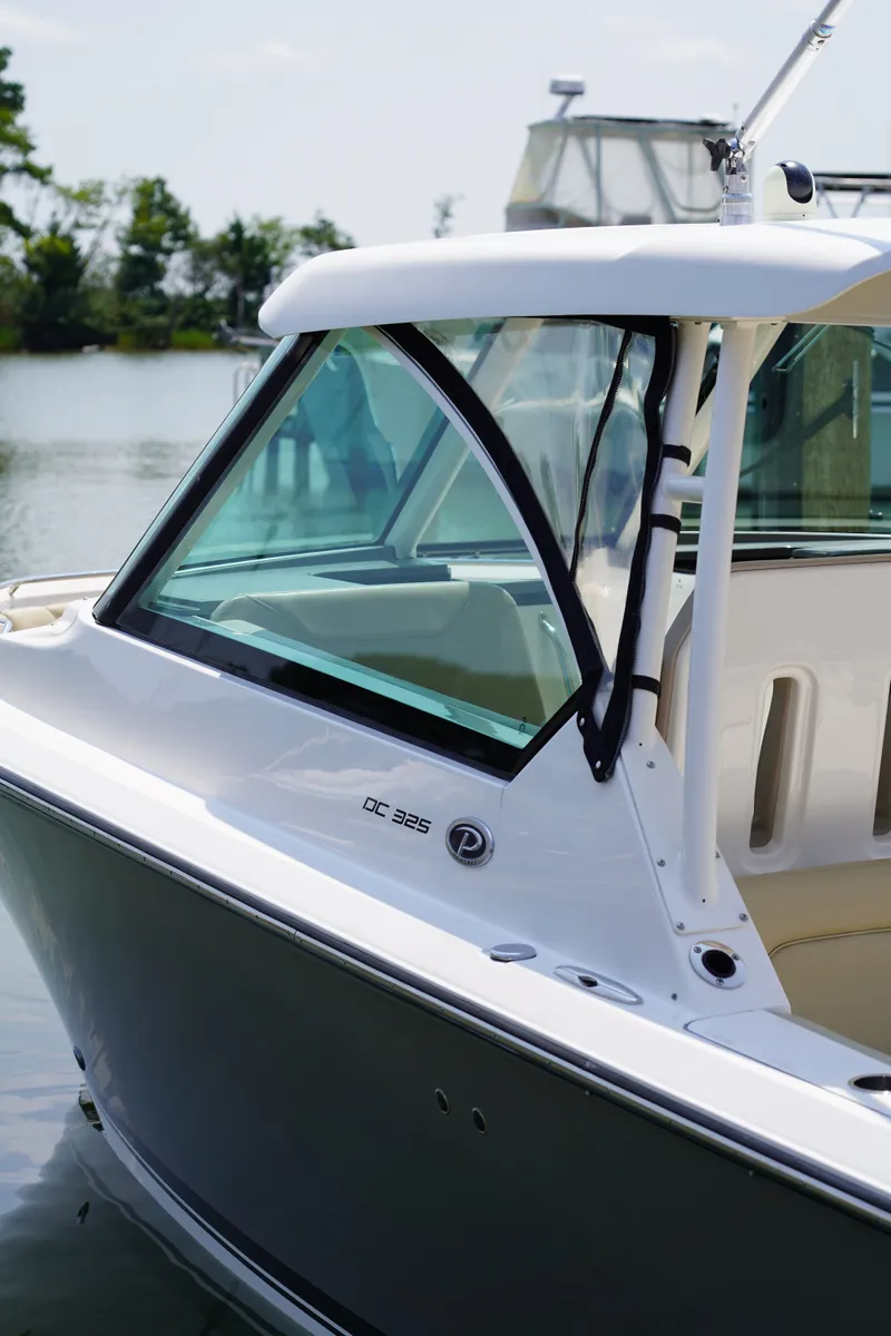 Slide: The Image of A 2015 Pursuit DC 325 Dual Console boat on the water with clear windows and a white roof. - 33