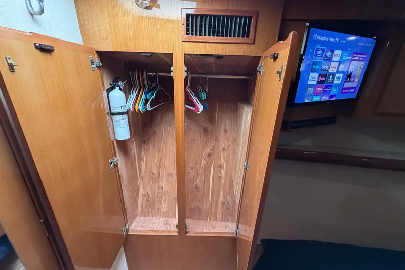 Slide: The Image of Open wooden closet with hangers and fire extinguisher, adjacent to a wall-mounted TV. - 80