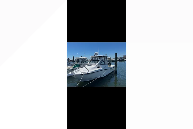 Slide: The Image of 2005 Boston Whaler 235 Conquest boat docked in a marina under clear blue skies. - 16