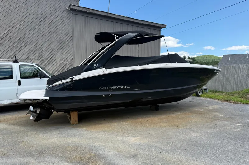 Slide: The Image of 2021 Regal LS6 boat with black cover, parked on a driveway beside a white van. - 1