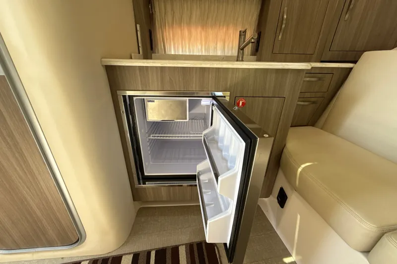 Slide: The Image of Open mini fridge in 2019 Regal 33 XO boat interior, featuring wood cabinetry and seating. - 23