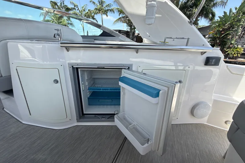 Slide: The Image of 2019 Regal 33 XO boat interior with open mini fridge, sleek design, and tropical backdrop. - 12
