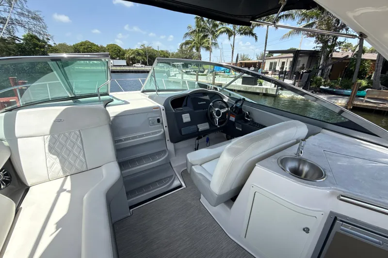 Slide: The Image of 2019 Regal 33 XO boat interior with helm, seating, and sink, docked by palm trees. - 14