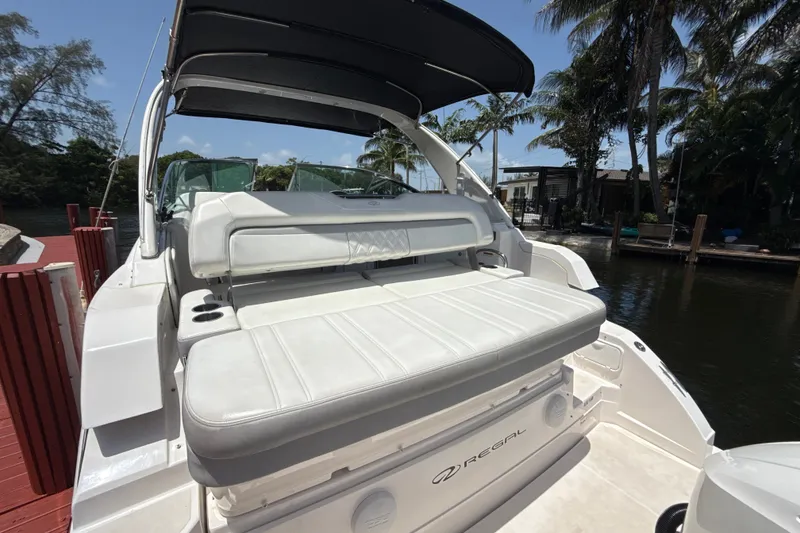 Slide: The Image of 2019 Regal 33 XO boat with white seating and canopy, docked by palm trees. - 6