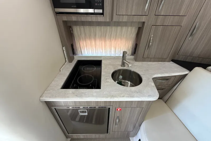 Slide: The Image of Compact kitchen area in a 2019 Regal 33 XO boat with stove, sink, and cabinetry. - 22