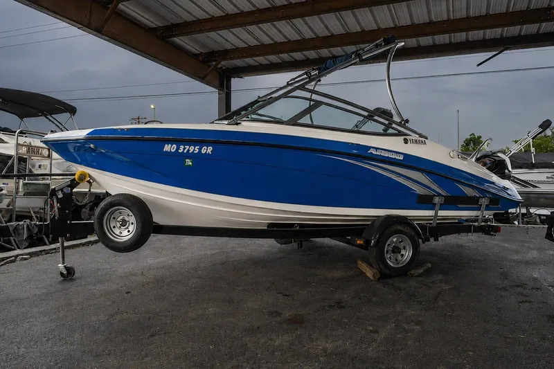 The Image of 2015 Yamaha Boats AR190 on trailer under shelter, blue and white design. - 1