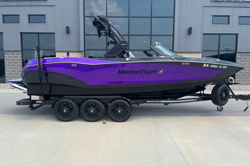 Slide: The Image of 2023 MasterCraft X24 boat in purple and black on a trailer, parked outside a building. - 3