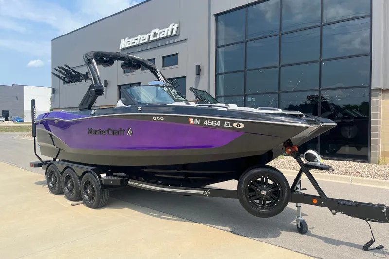 The Image of 2023 MasterCraft X24 boat in purple and black on a trailer outside a showroom. - 1
