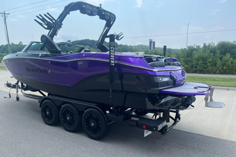Slide: The Image of 2023 MasterCraft X24 boat in vibrant purple on a trailer, parked outdoors. - 6