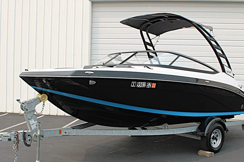 Slide: The Image of 2022 Yamaha Boats 195S on trailer, sleek black and white design, parked outdoors. - 1