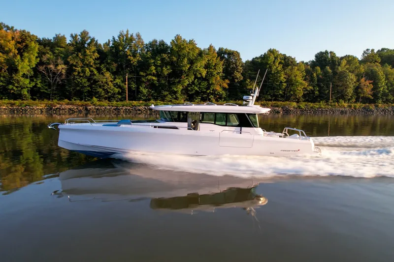 The Image of 2023 Axopar 45 XC Cross Cabin cruising on a calm river with lush forest backdrop. - 0