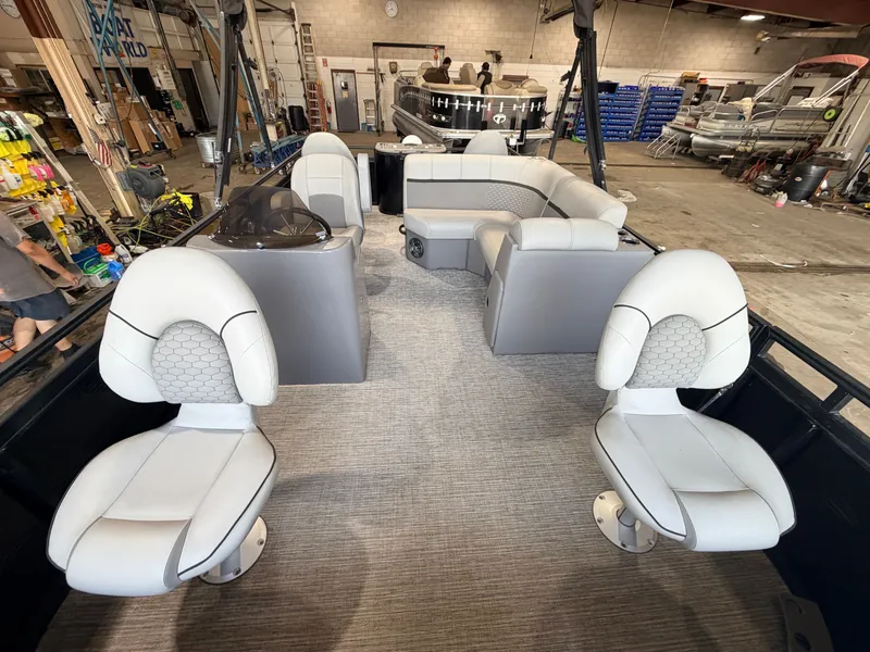 Slide: The Image of The image shows the interior of a 2023 Apex Marine Qwest L818 Fish with a 60HP Honda 4Stroke engine. There are two cushioned seats at the front and an L-shaped bench at the back. The floor is carpeted, and the boat is in a workshop. - 2