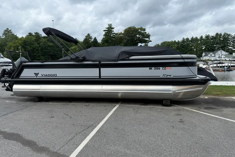 Slide: The Image of 2026 Viaggio X24 pontoon boat parked, covered, near a lakeside with trees in the background. - 13