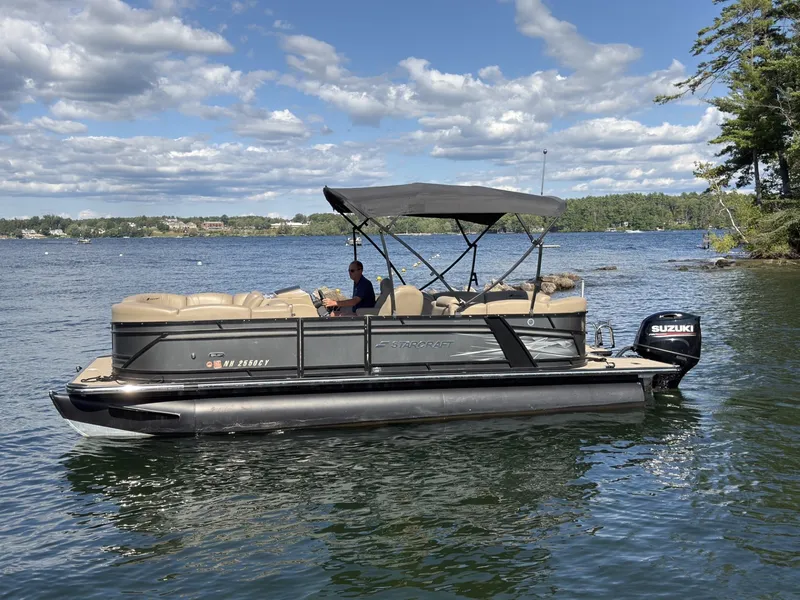 The Image of A 2019 Starcraft SLS 3 pontoon boat on a calm lake with a cloudy sky. - 1