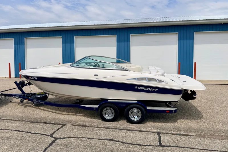 Slide: The Image of 2005 Starcraft 2100 IO RE Limited boat on trailer, parked near blue storage units. - 3