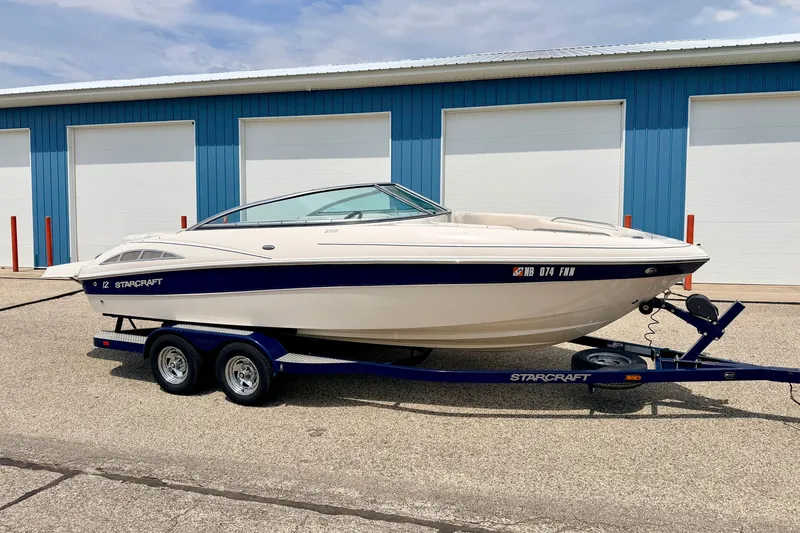 The Image of 2005 Starcraft 2100 IO RE Limited boat on trailer, parked near blue storage units. - 0