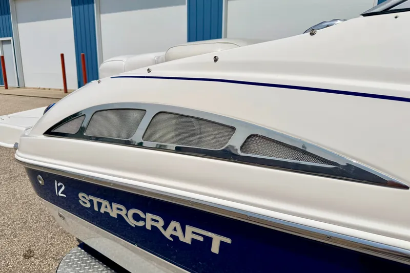 Slide: The Image of 2005 Starcraft 2100 IO RE Limited boat, white and blue exterior, docked near a building. - 15