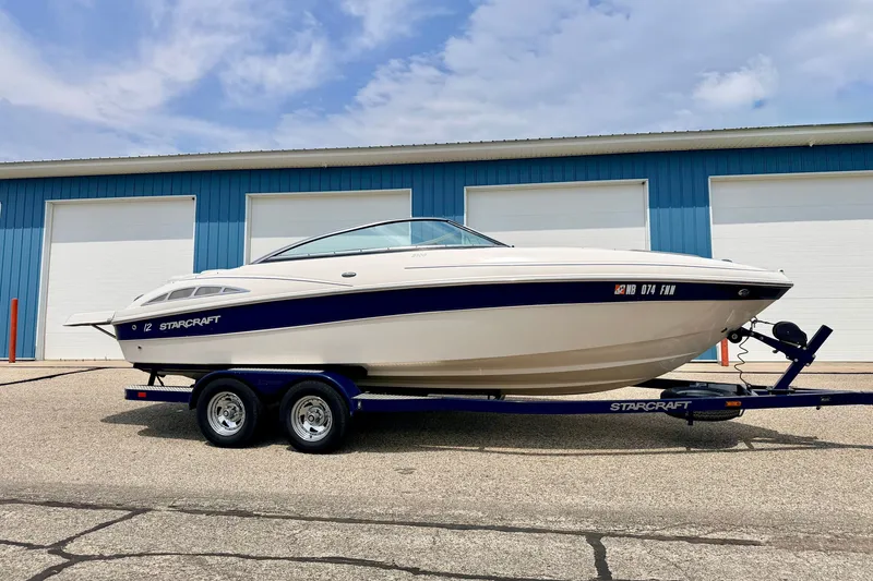 Slide: The Image of 2005 Starcraft 2100 IO RE Limited boat on trailer, parked outside blue building. - 4
