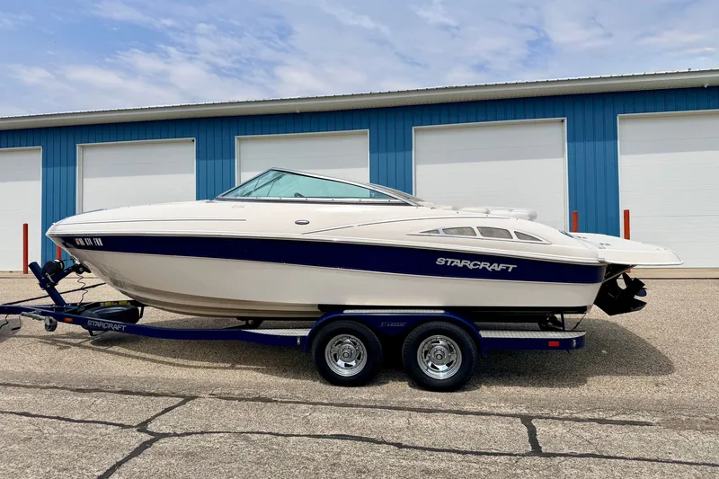 Slide: The Image of 2005 Starcraft 2100 IO RE Limited boat on trailer, parked near blue building. - 5