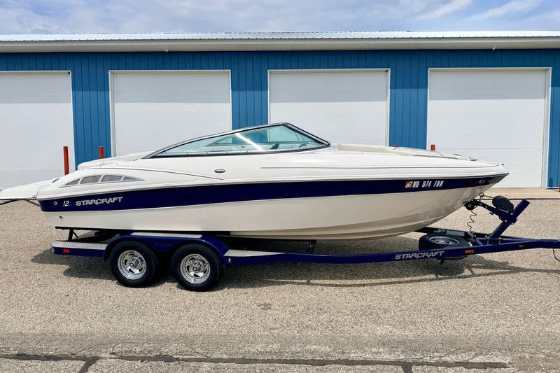 Slide: The Image of 2005 Starcraft 2100 IO RE Limited boat on trailer, parked near blue building. - 2