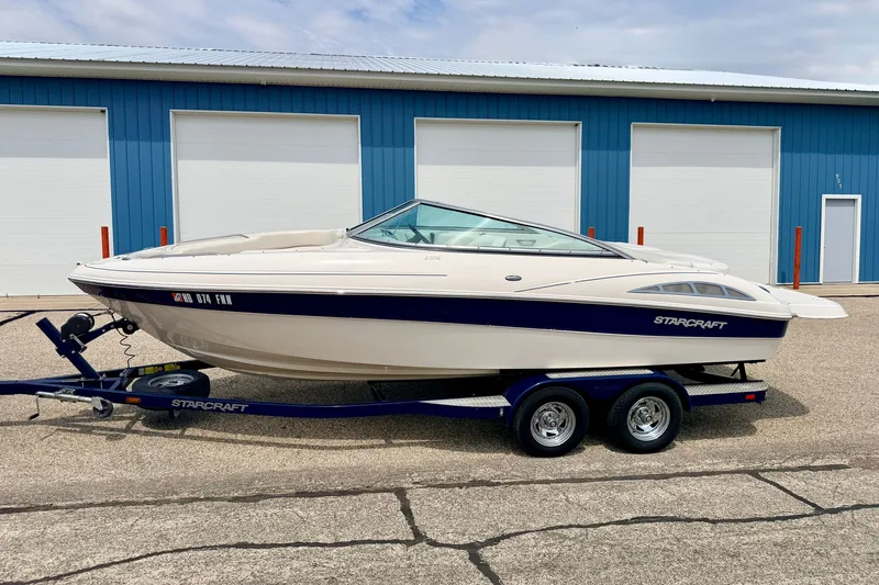 Slide: The Image of 2005 Starcraft 2100 IO RE Limited boat on trailer, parked outside blue building. - 1