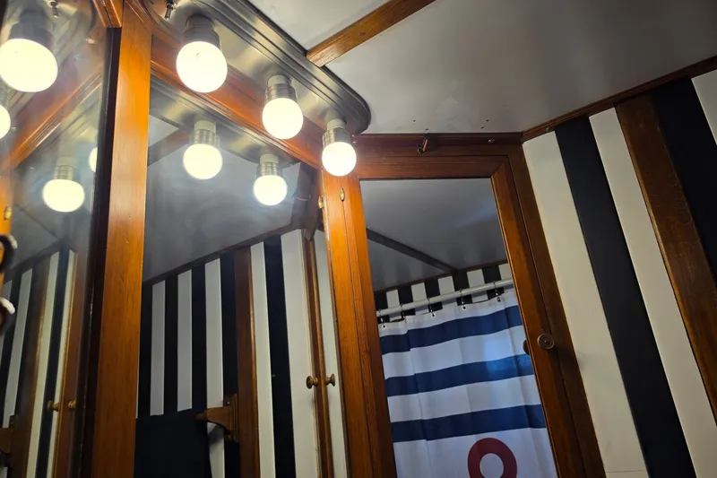 Slide: The Image of Vintage 1983 Monk 36 bathroom with striped walls, wooden cabinets, and bright vanity lights. - 19