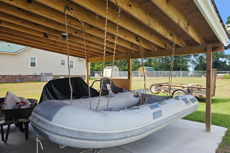 Slide: The Image of Hanging inflatable boat under wooden shelter, with yard and trailer in background. Monk 36, 1983. - 27
