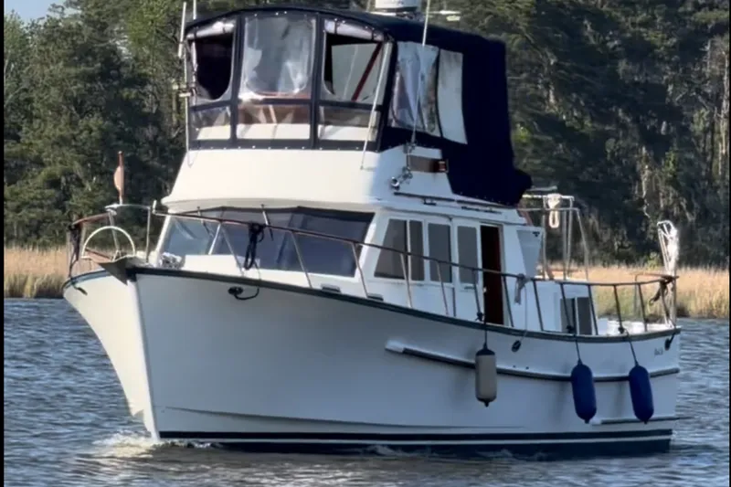 The Image of 1983 Monk 36 boat cruising on a serene waterway with lush greenery in the background. - 1