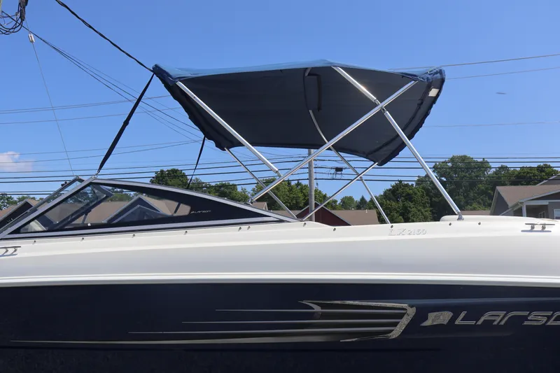 Slide: The Image of 2012 Larson LX 2150 boat with blue canopy, parked outdoors under clear sky. - 12