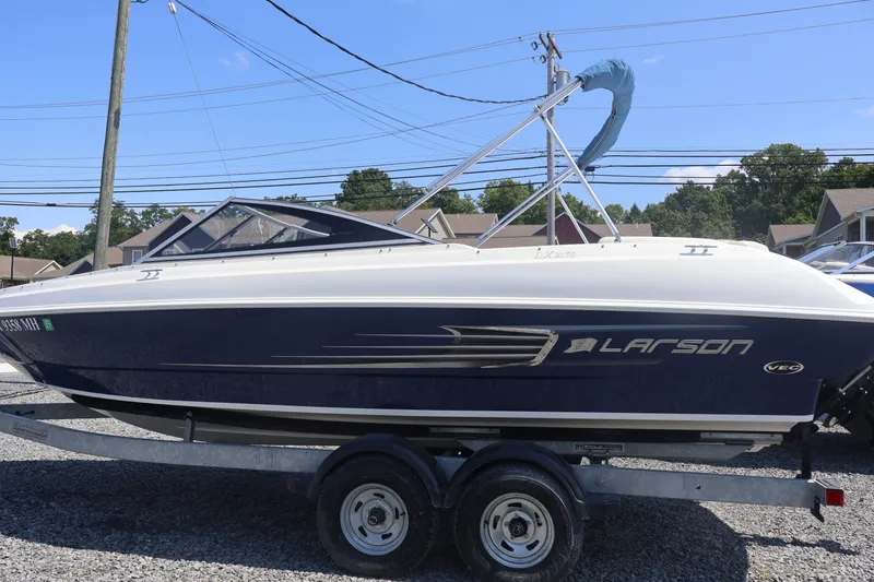 Slide: The Image of 2012 Larson LX 2150 boat on trailer, parked outdoors under clear blue sky. - 11