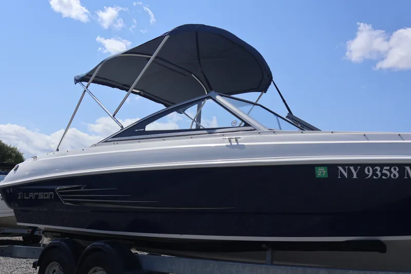 Slide: The Image of 2012 Larson LX 2150 boat with canopy, parked on trailer under blue sky. - 1