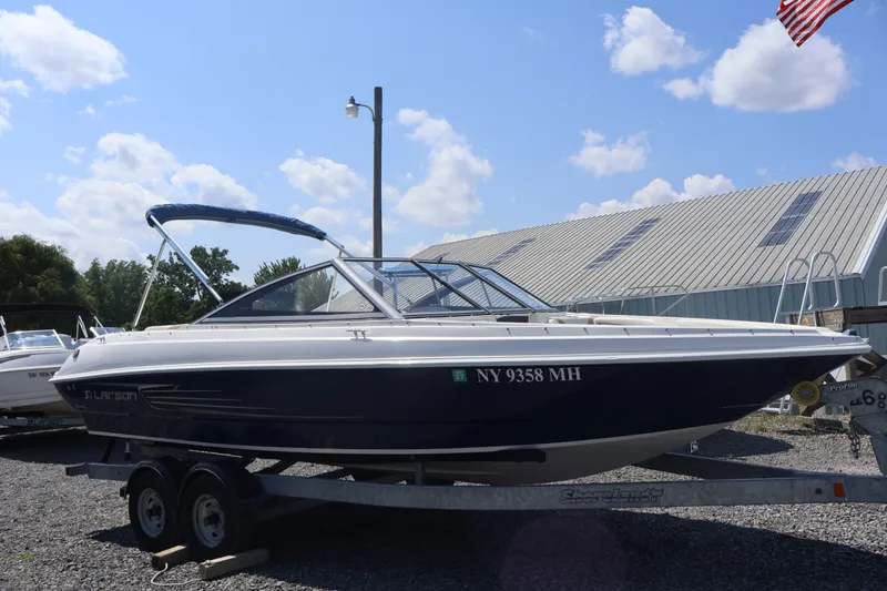 Slide: The Image of 2012 Larson LX 2150 boat on trailer, parked outdoors under blue sky. - 7