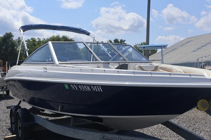 The Image of 2012 Larson LX 2150 boat on trailer, parked outdoors under a partly cloudy sky. - 0