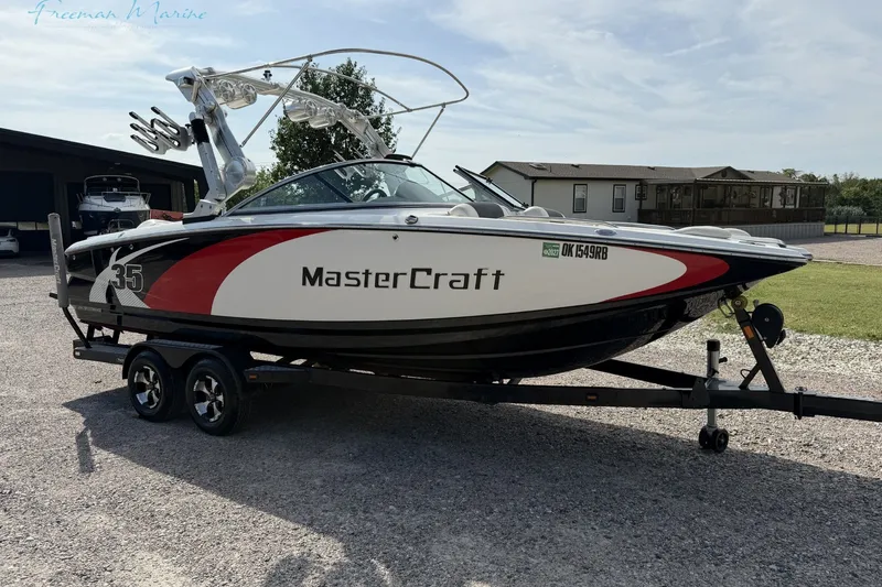 Slide: The Image of 2011 MasterCraft X-35 boat on trailer, parked outdoors, showcasing sleek design and vibrant colors. - 2