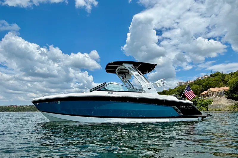 The Image of 2023 Cobalt R6 Surf boat on water, clear sky, American flag, scenic background. - 1