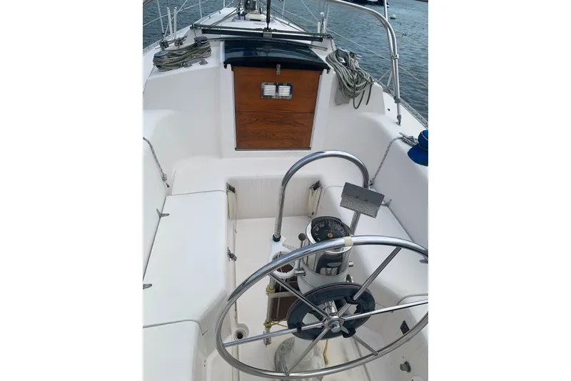 Slide: The Image of 1984 CS Sailcraft cockpit with steering wheel, compass, and wooden hatch, docked on calm water. - 2