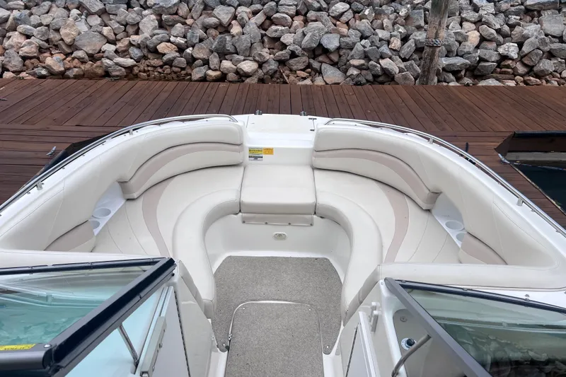 Slide: The Image of 2007 NauticStar 230 Sport Deck boat with spacious seating, docked by a rocky shoreline. - 5