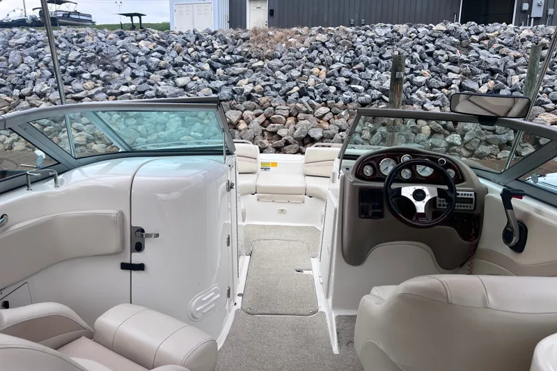 Slide: The Image of 2007 NauticStar 230 Sport Deck interior with steering wheel and seating, docked by rocky shore. - 13
