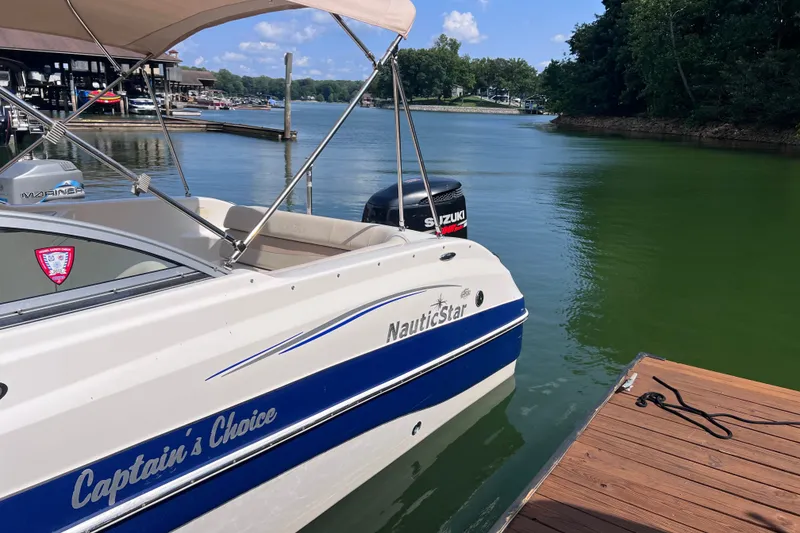 Slide: The Image of 2007 NauticStar 230 Sport Deck boat docked on a serene lake with clear skies. - 2