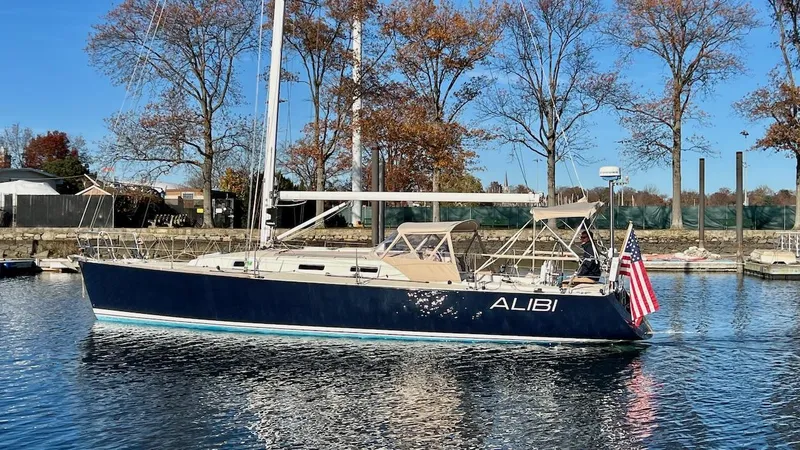 Slide: The Image of A 2000 J/120 sailboat with a blue hull and American flag, floating on calm water. - 35
